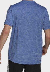 Sininen, lyhythihainen urheilupaita, joka on valmistettu rakenteellisesta, kosteutta siirtävästä kankaasta. Ominaisuuksiin kuuluu pyöreä kaula-aukko ja hieman pidempi takakäyrä.