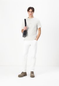 Light gray cotton t-shirt with small text, white tapered jeans, and tan ankle boots. Black crossbody bag adds contrast to the outfit.