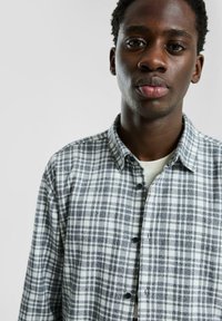 Koszula na guziki w biało-ciemnoszary wzór w kratę, z klasycznym kołnierzykiem i czarnymi guzikami. Miękka tkanina o swobodnym kroju.