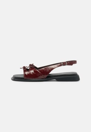 Burgundi odinės slingback basutės su plokščiu juodu padu, puikuojančios priekinės kaspinėlio detalės ir reguliuojama kulkšnies juosta. Lygus paviršius.
