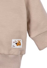 Beżowy bawełniany sweatshirt z prążkowanymi mankietami, kwadratową naszywką z rysunkowym psem i tekstem "How How How", dodający zabawnego akcentu.