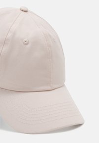 Lyserød baseballkasket lavet af tekstureret stof, med en buet skygge, syninger og en knap på toppen. Ingen synlige logoer.