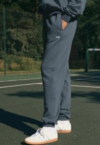 Grijze sweatpants met elastische boorden, zijzakken en een klein "self." logo. Draag ze met witte sneakers, voorzien van een gumrubberen zool en drie strepen.