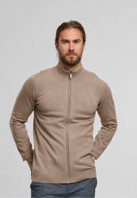 Maglione beige con zip, colletto alto e polsini a costine. Realizzato in materiale morbido, presenta una vestibilità aderente e un dettaglio logo discreto sul petto.