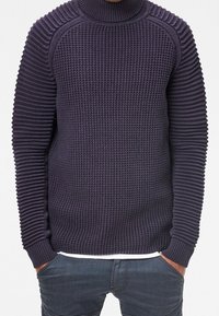 Mörkblå stickad tröja med hög krage, med texturerad ribbning på ärmar och kropp, samt en figurnära silhuett.