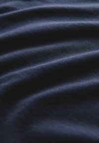 Sötétkék szövet, lágy textúrával, látható redőkkel és sima felülettel, kiemelve a rugalmasságát és fényességét.