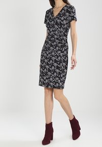 Blommig omlottskänning i mörk marinblått med korta ärmar, knälång klippning och en figurnära siluett; matchad med bordeauxfärgade anklarstövlar.