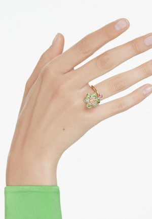 Flower-shaped ring with green and pink gemstones set in gold, featuring smooth surfaces and a slender band. Hand shown against a white background.
