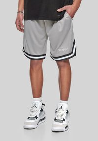 Shorts de sport gris avec des rayures noires et blanches, présentant une texture en maille et le texte "Dropsize" sur le côté. Associés à des baskets blanches et noires.