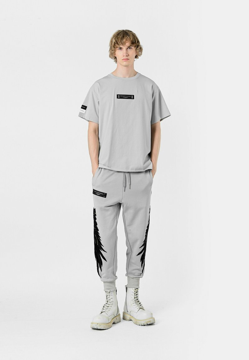 Camiseta gris de gran tamaño con detalle de etiqueta negra; pantalones de chándal grises a juego con patrón de plumas negras y bolsillos laterales; botas de combate blancas.