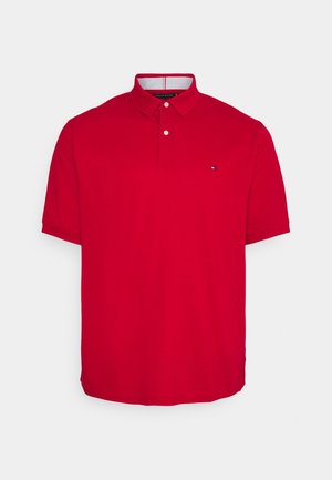 Polo rouge à manches courtes avec col à boutons et petit logo sur la poitrine gauche, présenté sur un fond gris clair uni.