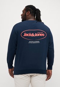 Dunkelblaues Sweatshirt mit langen Ärmeln. Verfügt über ein auffälliges pinkes "Jack & Jones"-Logo und den Text "Club 1990" auf der Rückseite. Hergestellt aus glattem Baumwollmischmaterial.