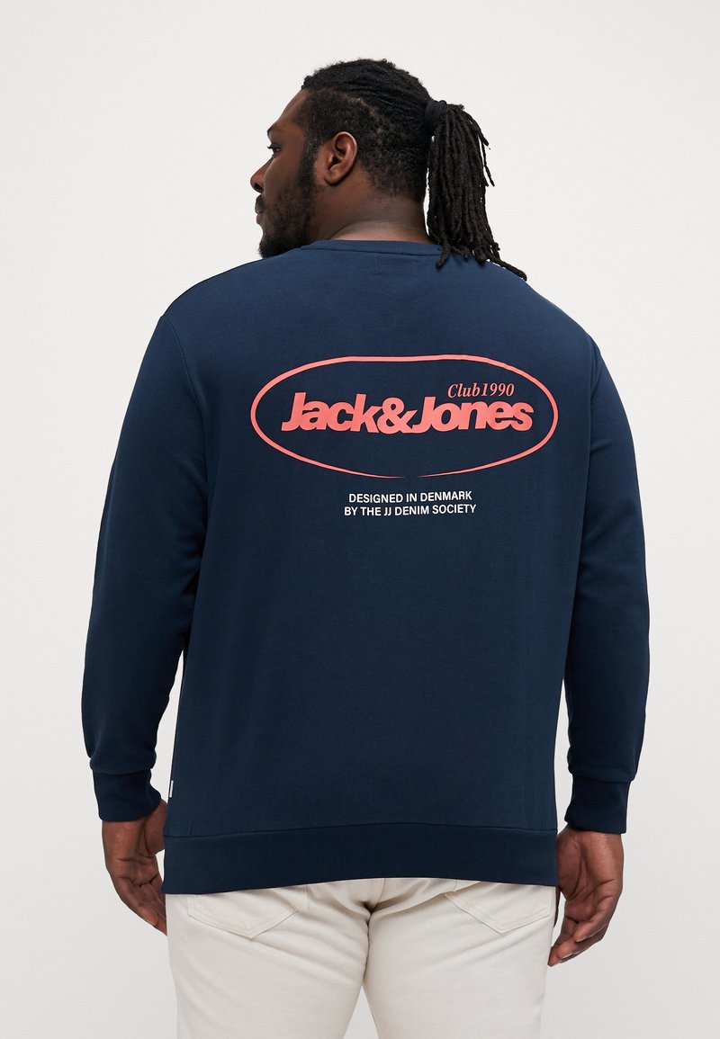 Dunkelblaues Sweatshirt mit langen Ärmeln. Verfügt über ein auffälliges pinkes "Jack & Jones"-Logo und den Text "Club 1990" auf der Rückseite. Hergestellt aus glattem Baumwollmischmaterial.