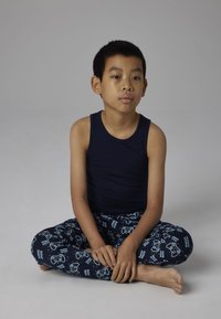 Débardeur marine associé à un pantalon de pyjama avec un motif de manette de jeu en bleu clair, fabriqué en tissu doux, au design ajusté, en position assise.