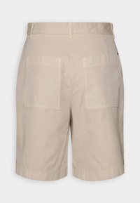 Shorts beiges arrivant aux genoux avec deux grandes poches arrière carrées et des passants de ceinture sur la taille, vus de derrière.