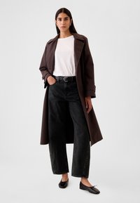 Ruskea trenssitakki valkoisen t-paidan päällä, yhdistetty korkeavyötäröisiin mustiin leveälahkeisiin farkkuihin ja mustiin balleriinoihin. Yksinkertainen muotoilu ja materiaalit.