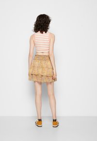 Top cropped listrado sem mangas em pêssego e branco, combinado com uma saia fluida e em camadas com um padrão floral em tons de amarelo e rosa. Usado com ténis.