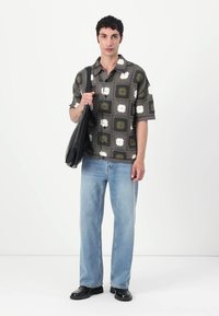 Cămașă cu mânecă scurtă, cu un model floral gri și măsliniu, asortată cu blugi ușori de denim albastru și pantofi negri, purtând o geantă neagră.