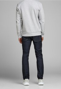 Felpa grigia con orlo a costine, jeans blu scuro e scarpe da ginnastica bianche. Vista posteriore che mette in evidenza la vestibilità dell'indumento e il contrasto dei colori.