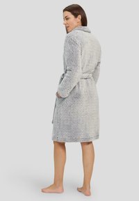 Bata de baño gris, texturizada, con detalle de cuello y cinturón. Presenta un patrón tejido y dos bolsillos laterales. Modelo visto desde la parte trasera.