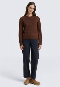 Brauner Strickpullover mit Rundhalsausschnitt und langen Ärmeln, kombiniert mit navy-blauen Hosen mit weitem Bein und beigen Knöchelstiefeln. Glatte Textur, lässige Passform.