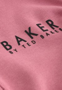 Nahaufnahme von rosa Stoff mit erhabenem schwarzen Text "BAKER BY TED BAKER" darauf gedruckt.