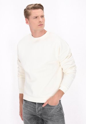 Cremefarvet sweatshirt med rund halsudskæring og ribbede manchetter, parret med grå denim jeans. Minimalistisk design uden synlige logoer.