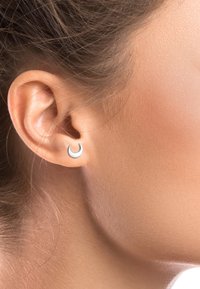 Silberner Creolenohrring in einer halbmondförmigen Form, mit glatter Textur und minimalistischem Design, im Ohr getragen, wobei die reflektierende Oberfläche hervorgehoben wird.