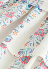 Biely textil s plisovaním, na ktorom je kvetinový vzor ružových, modrých a oranžových kvetov so zelenými listami.