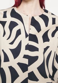 Top in tessuto beige caratterizzato da audaci motivi astratti in blu navy, con scollatura rotonda e dettaglio con spacco anteriore.