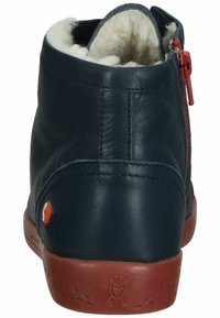 Botas de tobillo de cuero azul marino con un forro blanco de felpa, cremallera roja y logo naranja. Suela de goma con patrón de agarre texturizado.