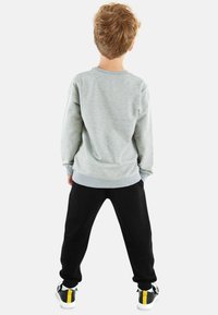 Grauer Sweatshirt mit geripptem Kragen und Bündchen, schwarze tapered Pants und schwarze Sneakers mit gelben Akzenten, von hinten betrachtet.