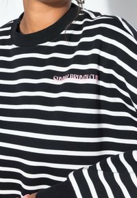 Chemise à manches longues rayée noir et blanc avec un col rond ; porte la broderie "SUNDAY BRUNCH CLUB" en rose sur la poitrine gauche.