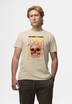 Beige katoenen t-shirt met een schedelafbeelding in donkerbruin en oranje, aangekleed met gele en roze graffiti-stijl tekst.