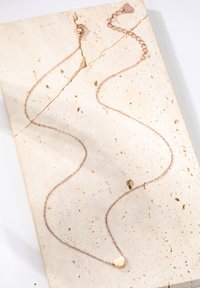 Collar de oro rosa con una delicada cadena y un pequeño colgante en forma de corazón, exhibido sobre una superficie de piedra texturizada. La cadena cuenta con un cierre de langosta.