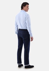 Helles blau gestreiftes Hemd mit Button-Down-Kragen, kombiniert mit dunkelblauen Jeans und schwarzen Slippern.