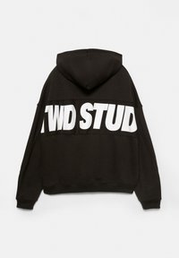 Sweat à capuche noir surdimensionné avec un texte blanc en gras « TWD STUD » sur le haut du dos et une grande capuche, sur un fond uni.