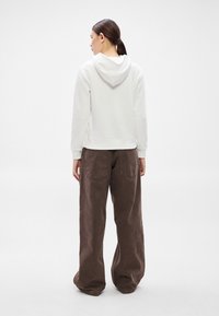 Hanorac alb cu glugă, cu un design scurt, asortat cu pantaloni maro, largi, cu talie înaltă și buzunare mari pe spate.