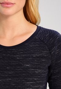 Laivastonsininen neulepaita, jossa on hienovarainen teksturoitu kuvio, pyöreä pääntie ja lyhyet raglan-hihat. Pehmeä kangas, jossa on kevyt kiilto.