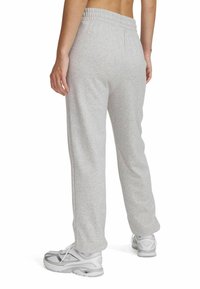 Grijze sweats voor heren van zacht materiaal, met een elastische tailleband, taps toelopende pijpen en een relaxed pasvorm. Draagt witte sportschoenen.