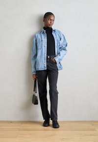 Veste en denim bleu clair, turtleneck noir, jeans noirs taille haute et baskets noires. Comprend un petit sac à main et un fond de mur texturé.