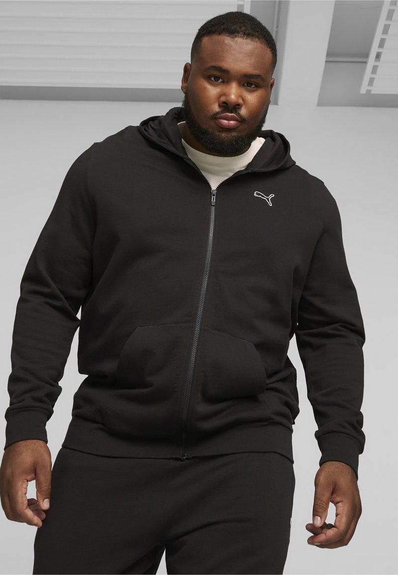 Sort zip-up hoodie lavet af blødt stof, med en kengurulomme, hætte og hvidt logo-accents på brystet.