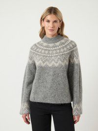 Grijze gebreide trui met een hoge nek, voorzien van een witte gebloemde yoke, ribbeltextuur en lange mouwen. Gecombineerd met zwarte broek.