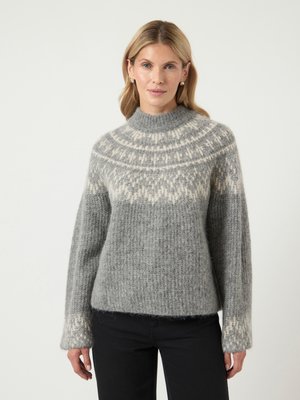 Grauer Strickpullover mit hohem Kragen, der eine weiße gemusterte Passe, gerippte Textur und lange Ärmel aufweist. Kombiniert mit schwarzen Hosen.