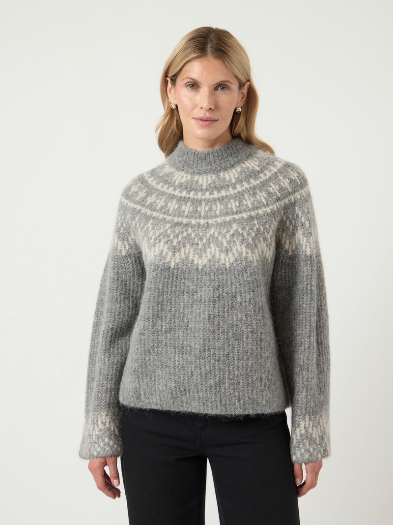 Suéter gris de punto con cuello alto, con un canesú blanco diseñado, textura acanalada y mangas largas. Combinado con pantalones negros.