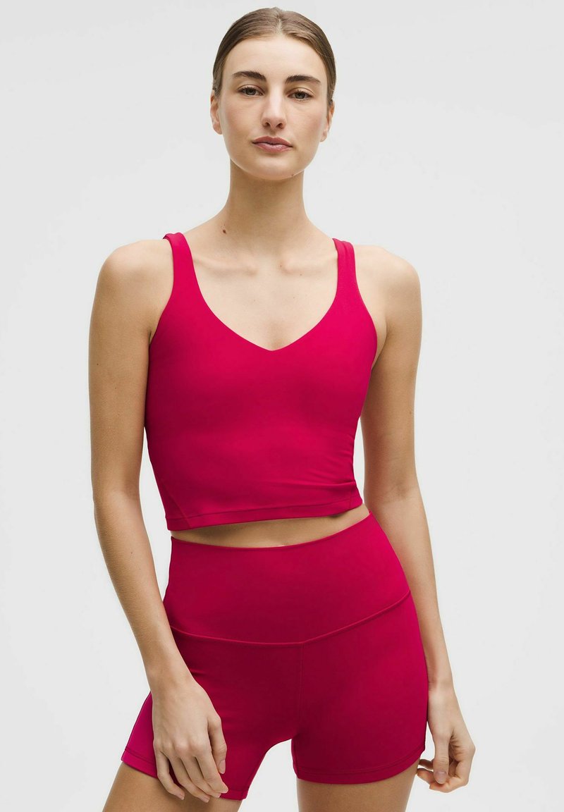 Red athletic crop top with a V-neck and thick straps, paired with high-waisted red shorts, both in a smooth, stretchy fabric.