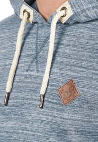 Sudadera gris-azul con una tela texturizada, presenta cordones de cuerda blanca, ojales de metal y una etiqueta de marca de cuero marrón.