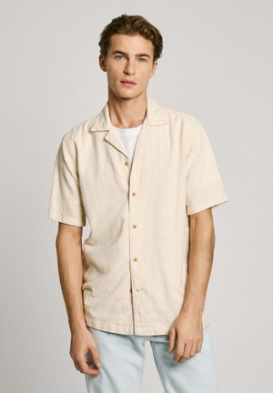 Beige overhemd met korte mouwen, voorzien van een gemêleerde structuur, met een kraag en vijf houten knopen, gecombineerd met lichtblauwe jeans.