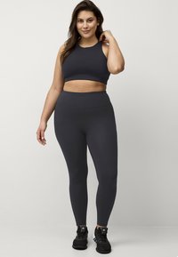 Mørkegrå atletisk cropped top og højtaljede leggings lavet af strækbart materiale. Komplementeret af sorte atletiske sko.