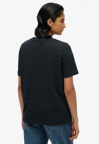 Donker marineblauw T-shirt met korte mouwen, een ronde hals, platte naden en een klein label vlak bij de kraag. Katoenen stof met een gladde textuur.